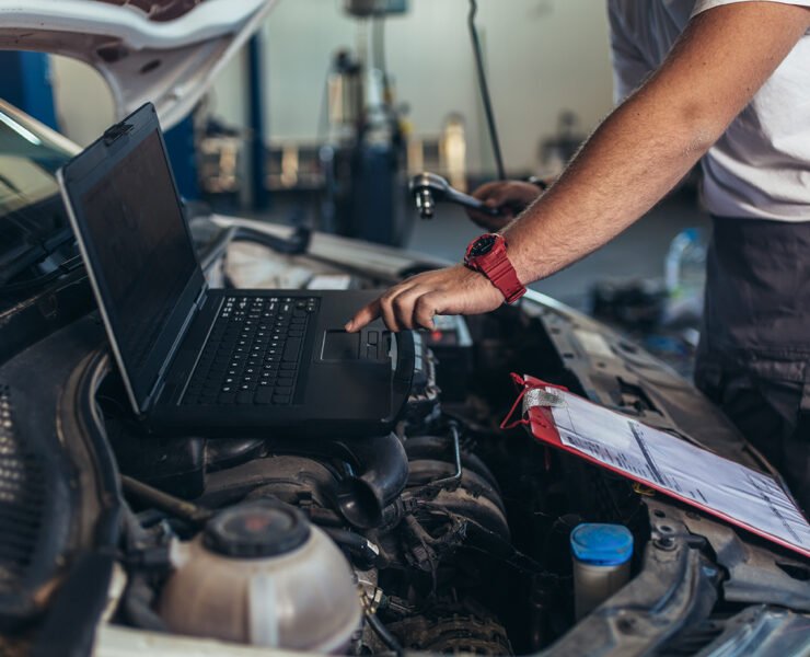 Professional car mechanic working in auto repair service using laptop.