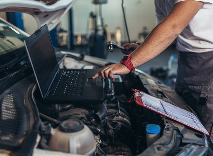 Professional car mechanic working in auto repair service using laptop.