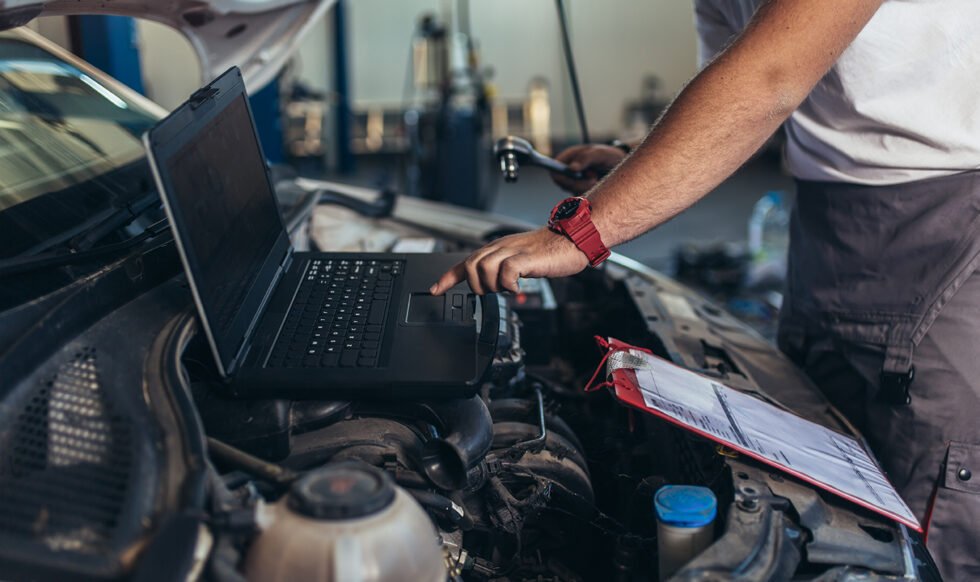 Professional car mechanic working in auto repair service using laptop.